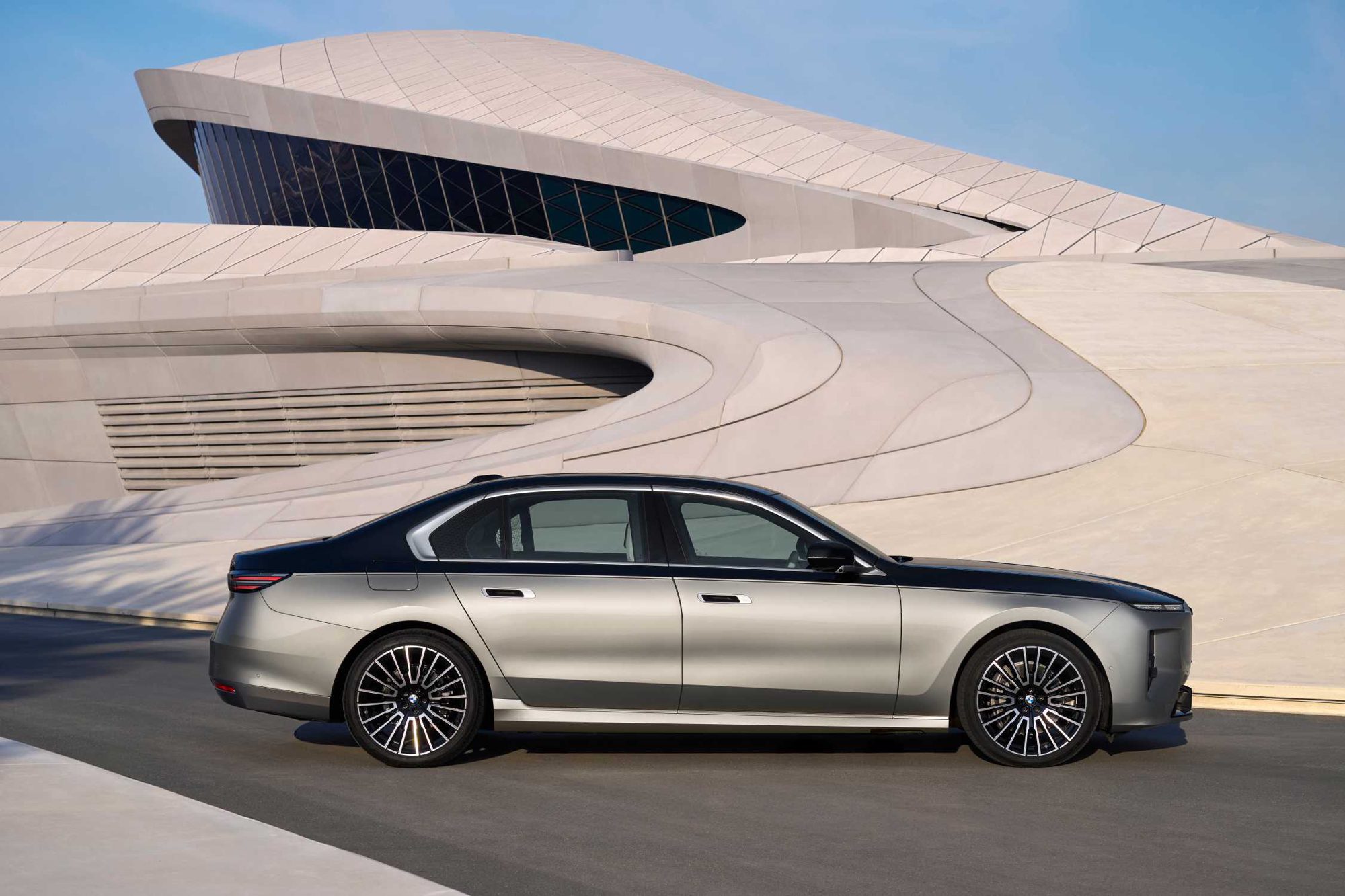 Ασημί BMW Σειρά 7 limousine σε πλάγιο προφίλ μπροστά από ένα καμπυλωτό λευκό κτίριο από σκυρόδεμα