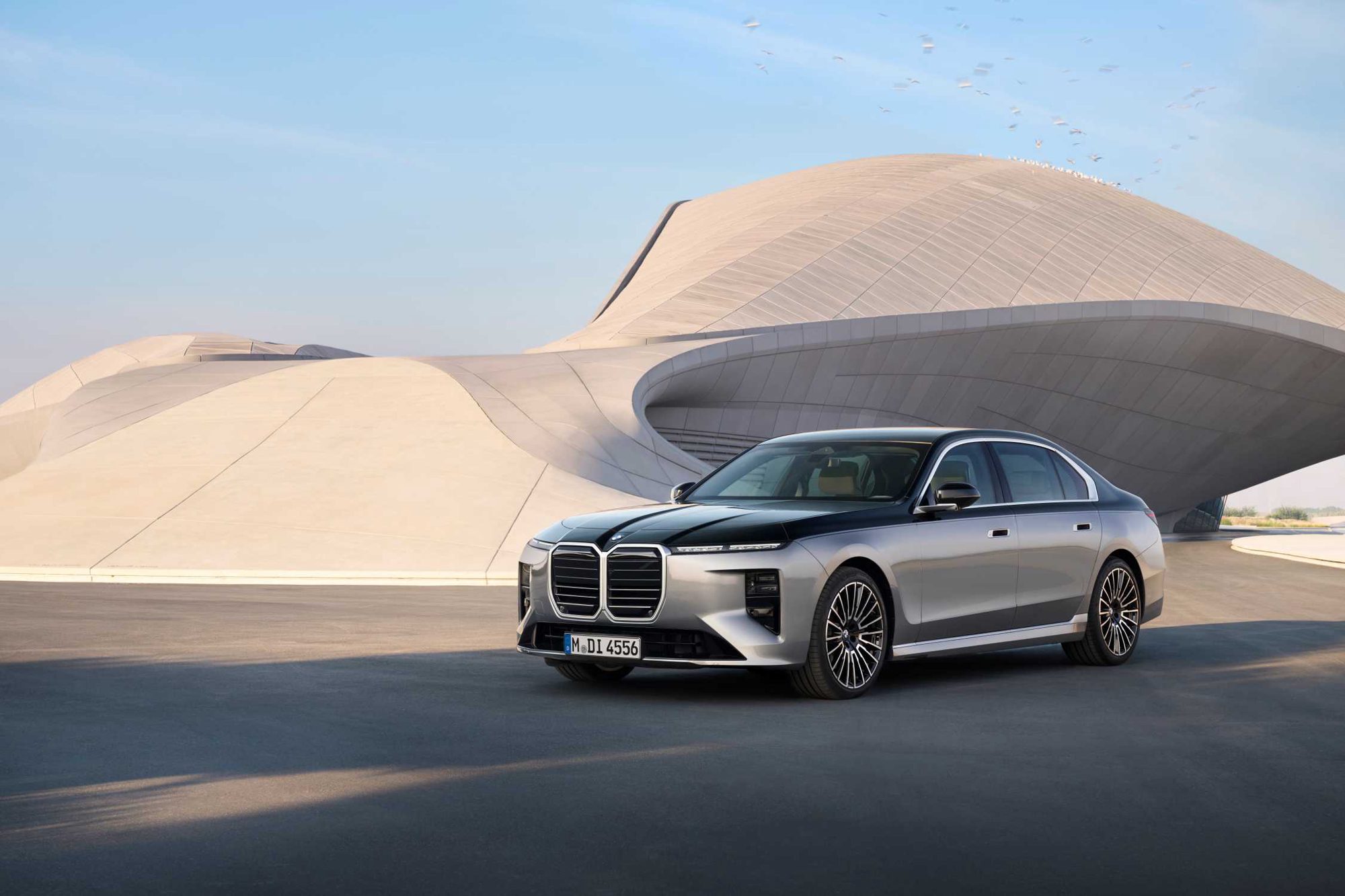 Berlina BMW Serie 7 vista diagonalmente da davanti davanti a un tetto di cemento curvo in ambiente luminoso